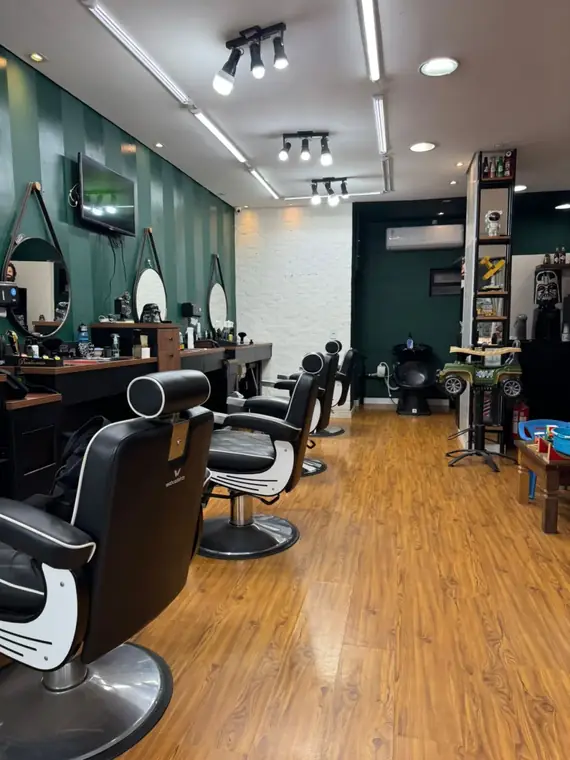Interior do salão da Los Barberos, com parede verde e cadeiras de barbeiro